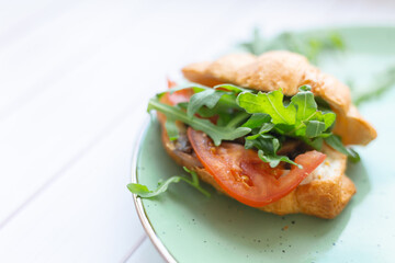Croissant with rocket salad and vegetables on a ceramic dish on a wooden table