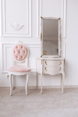 classic room with white patterned wall, dressing table with mirror, decorated with golden and pink soft chair. Details of the interior of the bedroom for girls and make-up, hairstyles with a mirror