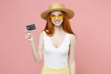 Young redhead rich happy caucasian woman 20s ginger long hair in straw hat glasses summer clothes holding credit bank card shopping online look overhead isolated on pink background studio portrait.