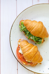 Two coissant with rocket salad and vegetables on a ceramic dish on a wooden table
