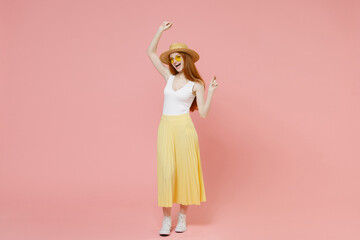 Full length body young fashionable redhead ginger woman in straw hat glasses summer clothes yellow pleated maxi skirt dancing raised up hand isolated on pastel pink color background studio portrait