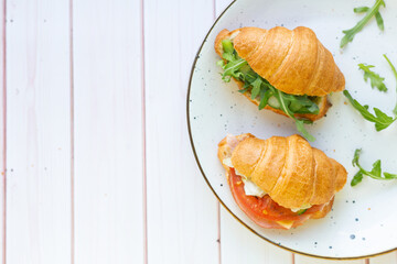 Two coissant with rocket salad and vegetables on a ceramic dish on a wooden table