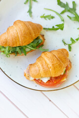Two coissant with rocket salad and vegetables on a ceramic dish on a wooden table