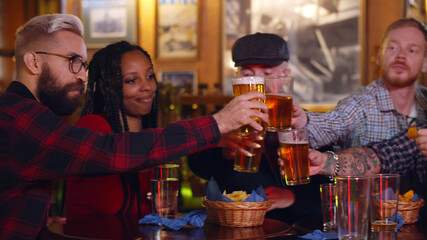 Young diverse people having fun together clinking beer pint in bar
