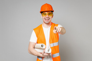 Smiling young handyman man in orange vest protective hardhat hold wallpaper rolls point index...