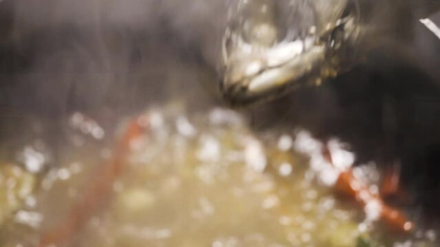 Someone put a fish on a boiling soup. Full of red chilli, lime leaf, scallion, galangal and lemongrass. Ingredient for a herbal soup. Thai food menu.