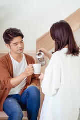 Young asian woman and man are enjoying spending time together at home with cup of coffee in hands.