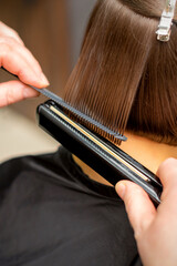 Close up of the hairdresser straightening the short hair of a female client with a hair straightening iron in a beauty salon