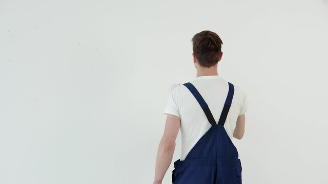 Painter with a roller in his hands paints a white wall. View from the back