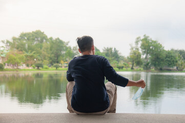 An Asian man takes off a mask Sit by the water along the way to the happy posture and then relax.
