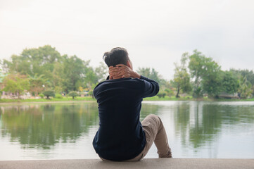 An Asian man sits by the water and then relaxes his way.