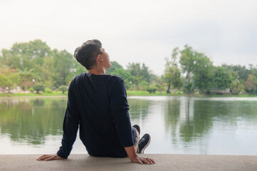 An Asian man sits by the water and then relaxes his way.