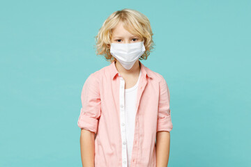 Little kid boy 10s in pink shirt sterile face mask safe from coronavirus virus covid-19 during quarantine isolated on blue turquoise background children studio portrait. Childhood lifestyle concept.