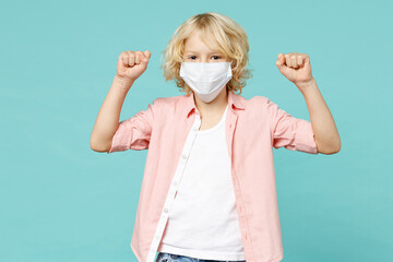 Happy little kid boy 10s in pink shirt sterile face mask safe from coronavirus virus covid-19 doing winner gesture isolated on blue turquoise background children portrait. Childhood lifestyle concept.
