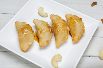 Bengali sweet - puli pitha in a white plate on wooden background with cashew nut and raisins.