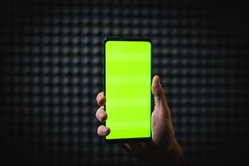 Holding black mobile phone with a green screen, isolated on a blurry dark background