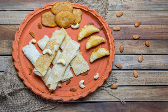 Bengali sweet - Patishapta Pitha, Malpua and Puli Pitha in a earthenware plate on wooden background with cashew nut, almonds and raisins.