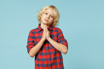 Pleading little curly kid boy 10s in red checkered shirt hold hands folded in prayer gesture,...