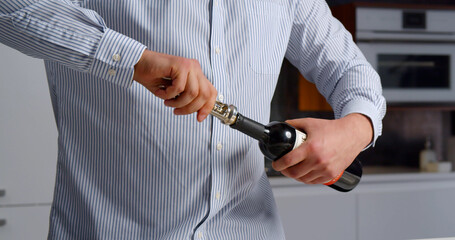 Young man opening bottle of wine while standing in kitchen at home