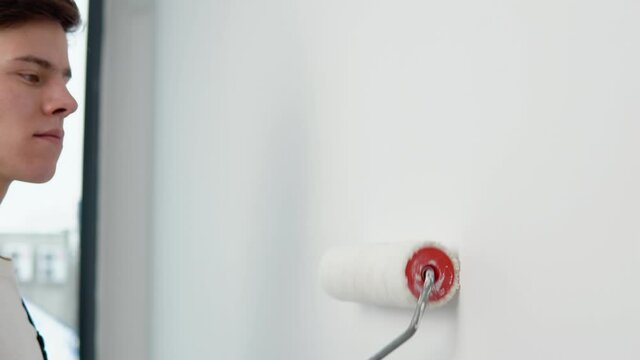 The painter paints the white walls with a paint roller