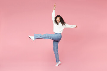 Full length young cute cheerful happy smiling african american woman 20s curly hair in white knitted sweater jeans raised up hand and leg fooling around isolated on pink background studio portrait. - obrazy, fototapety, plakaty