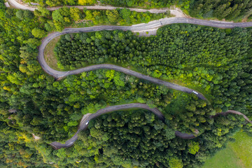 Aerial view of a winding countryside road passing through the green forest and mountain. White camping cars are passing through.
