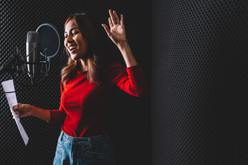 Pretty Asian female singer recording songs by using a studio microphone and pop shield on mic with...