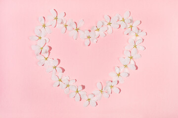 Shape heart laid out from flowers of white apple tree on pink backdrop. Holiday Mother's day, Valentine's Day, Wedding floral composition. Top view, flat lay. Horizontal orientation.