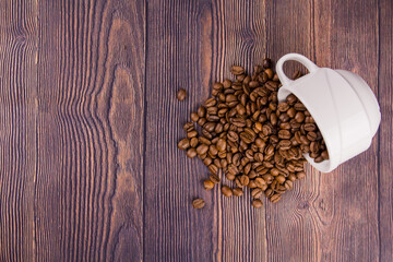coffee beans sprinkled from a white cup on a wooden table