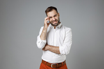 Worried puzzled young bearded business man wearing classic white shirt standing put hand on head looking camera isolated on grey color background studio portrait. Achievement career wealth concept.