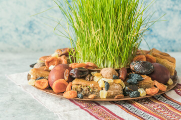 Novruz traditional tray with green wheat grass semeni or sabzi, sweets and dry fruits pakhlava on white background. Spring equinox, Azerbaijan copy space