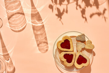 Heart shaped homemade cookies with strawberry jam on patel peach background with leaf shadows. Top view. Spring concept. Gluten free flour cookies