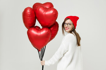 Obraz na płótnie Canvas Back rear view of young woman in sweater red hat glasses looking camera celebrating birthday holiday party hold bunch heart air inflated helium balloons isolated on white background studio portrait.