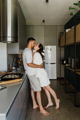 Young handsome man and woman hug and kiss while preparing pizza in the kitchen.