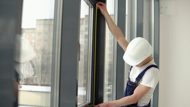 The window installer measures the dimensions of the window frame with a meter tape