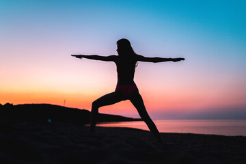 Silhouette of woman doing yoga at the beach at sunset during golden hour.