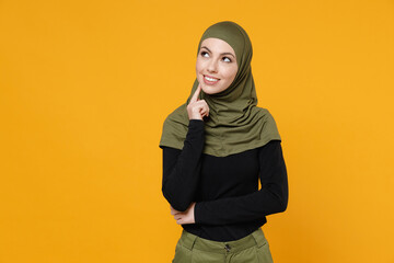 Pensive young arabian muslim woman wearing hijab black green clothes put hand prop up on chin looking aside up isolated on yellow color background, studio portrait. People religious lifestyle concept.