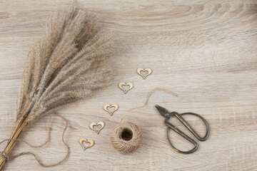 on a light wooden background miscanthus, rope, scissors and heart decor