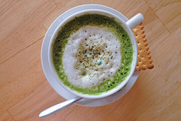 Top view of hot matcha green tea drink in a glass with spoon and biscuit