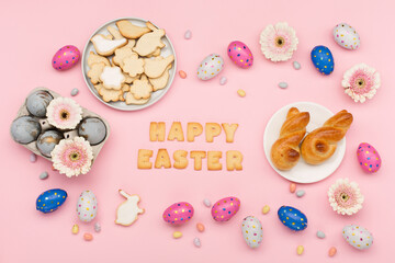 Homemade Easter bunny buns, sugar cookies, chocolate eggs, flowers on pastel pink background. Festive Easter breakfast concept.