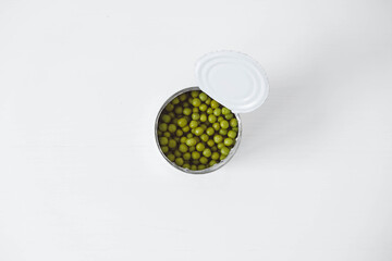 Canned green sweet peas in an open aluminum metal can on a white table. Top view. Copy, empty space for text