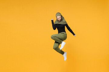 Full length joyful young arabian muslim woman wearing hijab black green clothes jumping doing...
