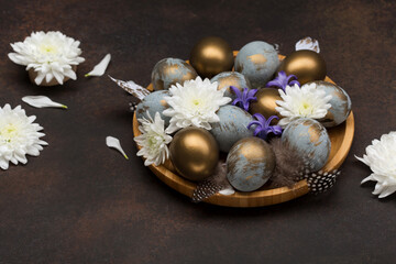 Fototapeta na wymiar Easter Decoration with gray blue golden eggs, quail feathers, white flowers on dark wooden background. Selective focus, copy space.