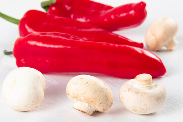 red bright sweet bell peppers and white fresh champignons on white wooden table