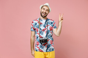 Naklejka premium Excited young traveler tourist man in summer clothes hat with photo camera showing victory sign isolated on pink background. Passenger traveling abroad on weekends getaway. Air flight journey concept.
