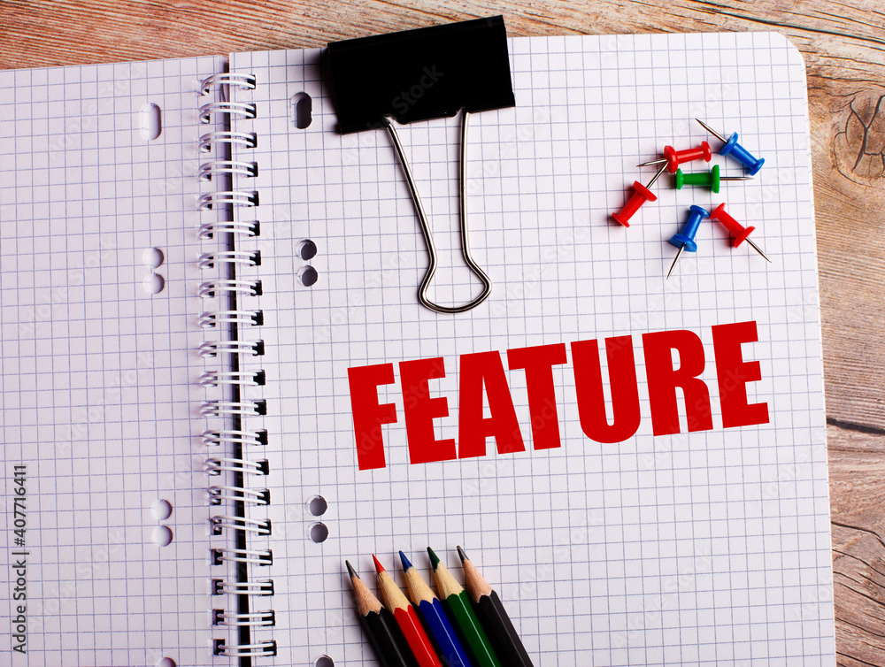 Poster the word feature is written in a notebook near multi-colored pencils and buttons on a wooden backgro