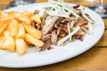 Griechisches Schweinefleisch Gyros mit Zwiebeln, Tsatsiki und Pommes auf Holz Tisch in Restaurant
