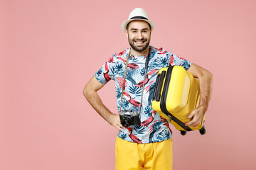 Smiling young traveler tourist man in summer clothes hat photo camera hold suitcase isolated on pink background studio portrait. Passenger traveling abroad on weekends. Air flight journey concept.