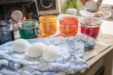 Frau taucht gekochte Eier mit Löffel in bunte Ostereier Kaltfarben in Rot, Orange, Gelb, Blau, Grün in Glas auf Papier Unterlage in Küche zum Färben zu Ostern
