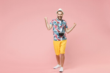 Full length of joyful young traveler tourist man in summer clothes hat doing winner gesture celebrating say yes isolated on pink background. Passenger traveling on weekend. Air flight journey concept.